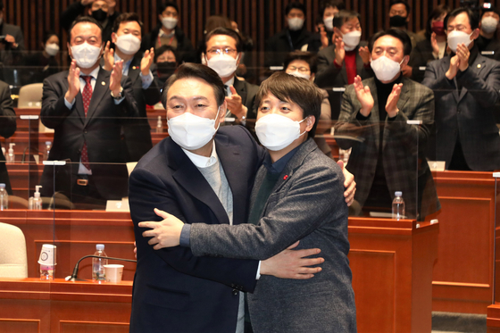 People Power Party (PPP) chairman Lee Jun-seok, right, and PPP presidential candidate Yoon Suk-yeol hug after they resolve their weeks-long feud during a party meeting at the National Assembly in western Seoul on Thursday evening. [JOONGANG PHOTO]