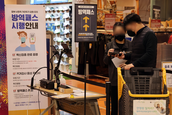A shopper flashes a QR code to prove vaccination status upon entry to an Emart in Seoul on Wednesday. Under the strengthened vaccine pass policy, which went into effect Monday, large supermarkets and department stores require all customers to have vaccine passes for entry. [YONHAP] 