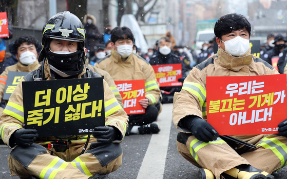 Firefighters stage a rally near the presidential office Blue House in central Seoul on Monday, holding up pickets reading “We don’t want to die anymore” and “We are not firefighting machines.” [NEWS1]