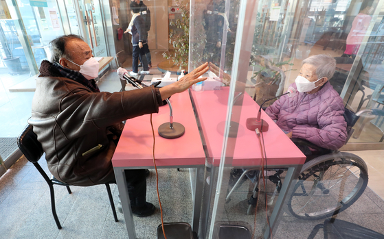 A woman and her husband greet each other through a glass wall divider at a nursing hospital in Daejeon on Tuesday. [YONHAP]