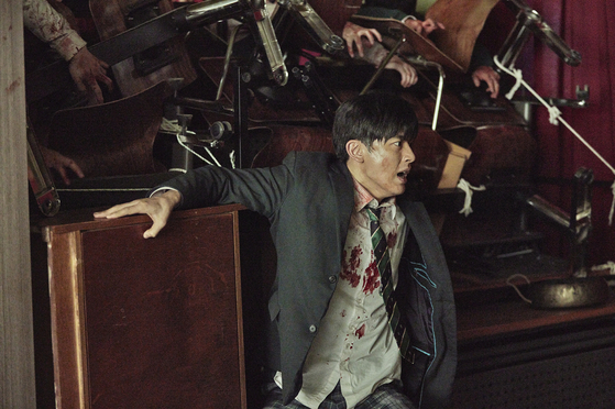 Character Lee Soo-hyuk (played by Lomon) tries to prevent a pack of zombies from entering with stacks of chairs and desks. [NETFLIX]              