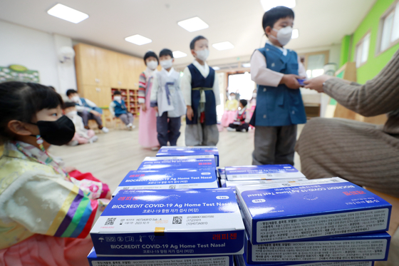 Children dressed in hanbok at a kindergarten in Busan receive Covid-19 self-testing kits from a teacher on Thursday ahead of the Lunar New Year holiday. [YONHAP]