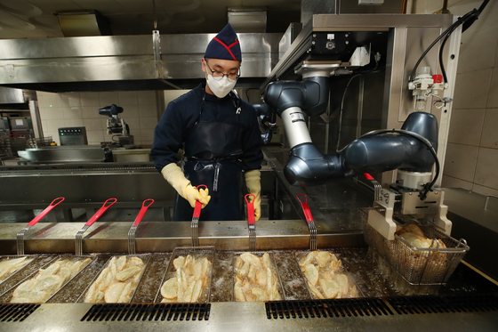 A soldier chef demonstrates frying dumplings with a cooking robot at an army boot camp in Nonsan, South Chungcheong, on Monday. Cooking robots operating under standardized cooking procedures have improved the quality of meals, the military boot camp said. [YONHAP]