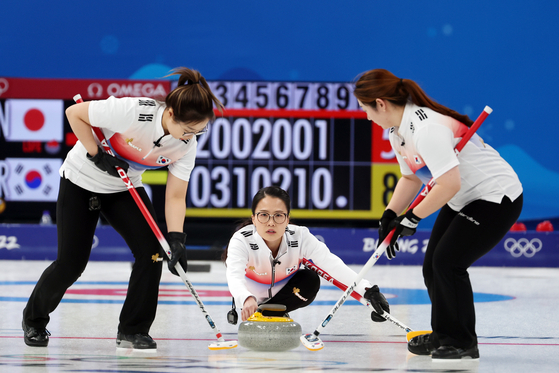 Kim Eun-jung, center, slides a stone during a round robin match against Japan at the National Sliding Centre in Beijing on Monday. [JOONGANG ILBO]