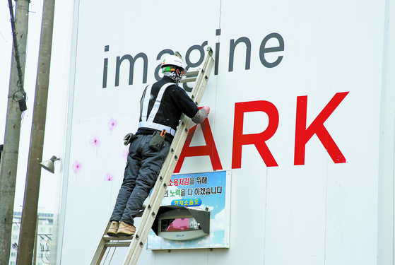 A worker erases the word ″Ipark″ from a hoarding on a construction site on Feb. 1. Ipark is the apartment brand of Hyundai Development Company, and people have been reluctant to move into its apartments after a HDC-built building collapsed in January. [YONHAP] 