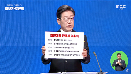 Ruling party candidate Lee Jae-myung holds up a board with a portion of the transcript of a recorded conversation where Kim Man-bae, owner of Hwacheon Daeyu, alleged Yoon Suk-yeol would ″die″ if Kim showed the ″cards″ he holds. [MBC]