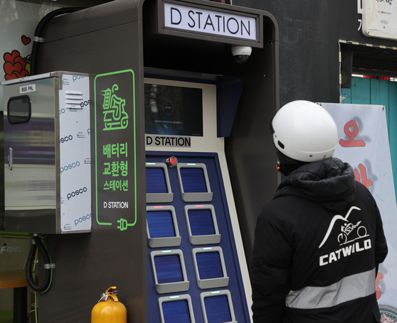 A delivery worker looks at a battery swap station at a CU branch in Seodaemun District, western Seoul, on Monday. BGF Retail's convenience store chain CU introduced the battery swap service for electric motorcycles at some of its branches on Monday. [YONHAP] 