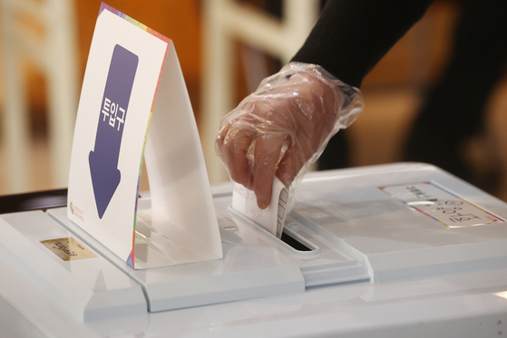 A voter is putting the ballot in the box while wearing a single-use plastic glove for the 20th presidential election in Gwangjin District, eastern Seoul, Wednesday. [YONHAP]