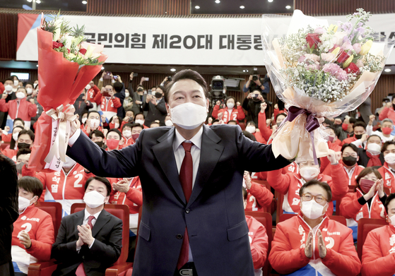 Yoon Suk-yeol of the conservative People Power Party (PPP) holds up bouquets after he was confirmed president-elect early Thursday at the National Assembly in Yeouido, western Seoul. [YONHAP]