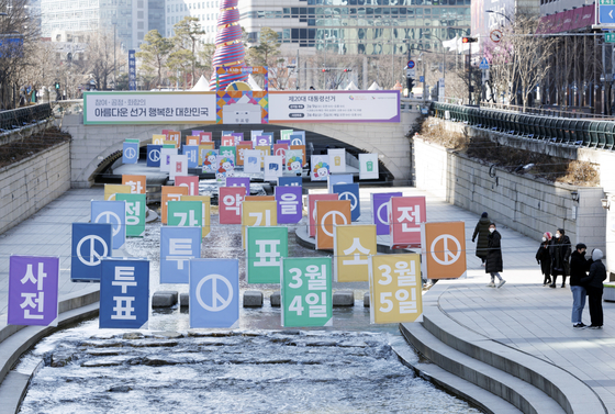 Pedestrians walk past signs advertising the advance voting period for the March 9 presidential election to be held on March 4 and 5 at the Cheonggyecheon in central Seoul on Sunday. [YONHAP]