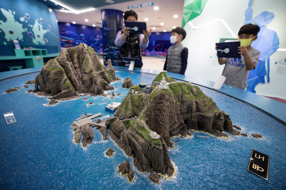 Visitors to a national library in Gangnam District, southern Seoul, on Wednesday view a model of the Dokdo islets, called the Takeshima islets in Japan, in the East Sea. Some Japanese history textbooks for high school students next year say the islets are Japanese territory, drawing a protest from the Korean Foreign Ministry. [NEWS1]