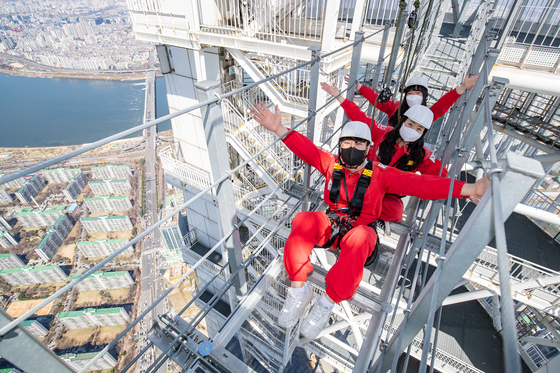Customers take the Sky Bridge Tour at the Lotte World Tower in southern Seoul. The tour, which involves walking across a bridge 54 meters (177 feet) in the air, reopened after it was halted in the winter, Lotte Shopping said Thursday. [YONHAP]