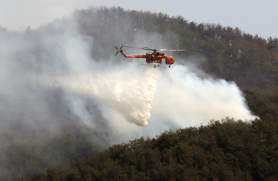 A helicopter flies over a fire in Yanggu, Gangwon on Monday afternoon as efforts to extinguish a blaze that began Sunday continued. [YONHAP]