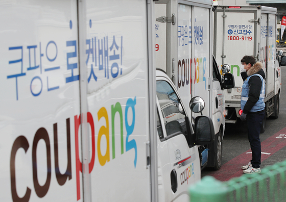 A Coupang delivery worker stands by one of the company's delivery trucks. [YONHAP]