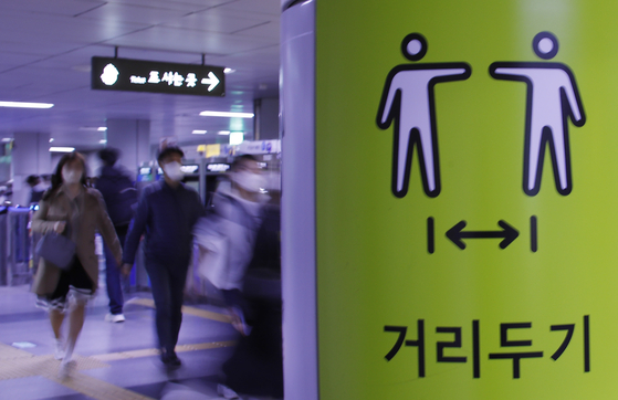 People walk in City Hall station past a poster promoting social distancing. From April 18, many social distancing restrictions will be lifted. [NEWS1]