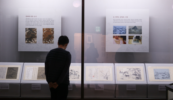 A visitor looks at cultural heritages that have recently completed receiving preservation treatments at the "Bohwasubo" exhibit, the first exhibit in seven years at the Kansong Art Museum, also known as Bohwagak, in Seongbuk District, central Seoul, on Friday during the exhibit's pre-opening. [YONHAP]