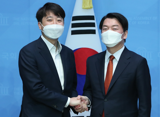Lee Jun-seok, chairman of the People Power Party (left) and Ahn Cheol-soo, leader of the People’s Party (right) shake hands after announcing the merger of the two parties at the National Assembly on Monday. [NEWS1]
