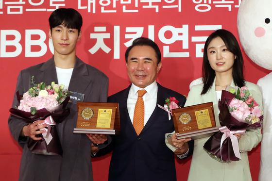 Short-track speed skating gold medalists Hwang Dae-heon, left, and Choi Min-jeong, right, pose for a photo after receiving a plaque from Genesis BBQ chairman Yoon Hong-geun at the Lotte Hotel Seoul on Thursday. Genesis BBQ, the operator of fried chicken chain BB.Q Chicken, will provide Olympic gold medalists with membership reward points worth 30,000 won ($24) every day until they turn 60. [NEWS1]
