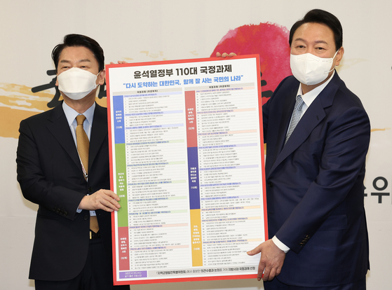 Ahn Cheol-soo, head of the transition team, left, and Yoon Suk-yeol, president elect, hold up a list of 110 national projects at the transition team's headquarters in Jongno, Seoul, on Tuesday. [YONHAP] 