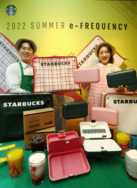 Starbucks Korea employees pose with this year’s e-frequency merchandise including a carry-on bag, cabin bag and a wearable blanket hoodie. Customers can get these items using their e-frequency points, which is a stamp-based loyalty scheme. The event starts May 10. [YONHAP]