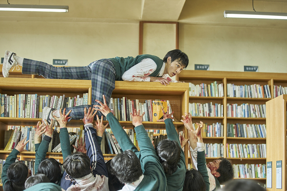 Character Lee Chung-san, played by Yoon Chan-young, tries to evade zombies by crawling on top of a bookshelf in the school library. [NETFLIX]