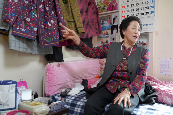 Noh Jeong-woo, a 77-year-old living on her own in western Seoul, sits on her bed with SK Telecom's Nugu AI smart speaker on her bedside. [SK TELECOM]