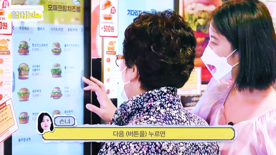 A granddaughter shows her grandmother how to use a kiosk at a fast food restaurant. [JOONGANG PHOTO]