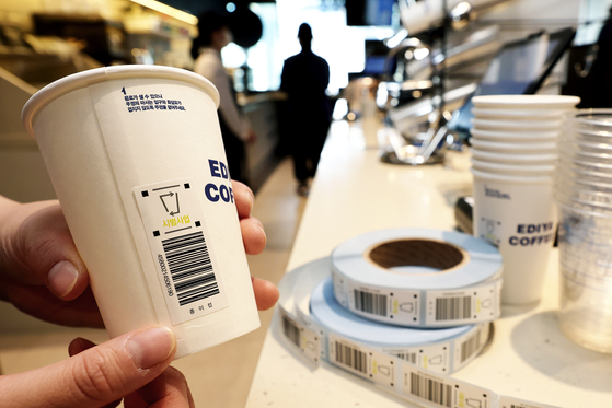 An Ediya Coffee employee shows the barcode sticker on a single-use paper cup, promoting the regulation that will be implemented in December. [JANG JIN-YOUNG]