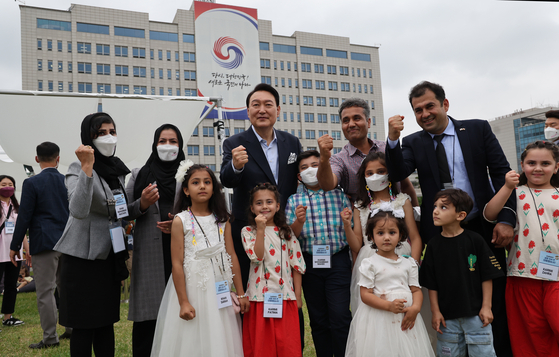 President Yoon Suk-yeol, center, takes a photo with Afghans settled in Korea at an event celebrating the presidential office’s move to Yongsan District in central Seoul Sunday. The event was attended by some 400 people including residents of the neighborhood, small merchants hit by Covid-19 and Afghans evacuated to Korea last year. [YONHAP]