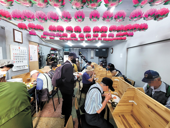 People eat the free meals served at a free cafeteria at Wongaksa in Jongno District, central Seoul, on Friday. [SUK GYEONG-MIN]