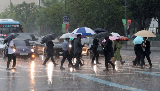 People holding umbrellas cross a main street in downtown Seoul on Thursday as the rainy season begins.  [NEWS1]
