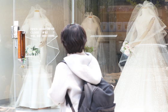 As Covid-19 social distancing measures end, many young couples who have delayed weddings are rushing to tie the knot. A person passes wedding dress shops in Mapo District, western Seoul.