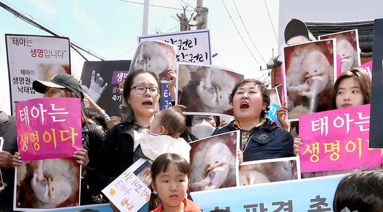 Left: Anti-abortion activists stand outside the Constitutional Court in central Seoul on April 11, 2019, holding cards reading ″We urge for the abortion law to be kept.″ [NEWS1]