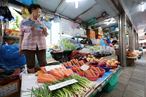 A grocery store owner looks over the vegetables while holding a fan, at a traditional market in Seoul on Sunday. Consumer prices for the month of June, which will be announced in the coming week, are expected to have increased by over 6 percent, according to market insiders. Prices will likely display a sharper hike in July and August with gas and electricity bills rising. [YONHAP]