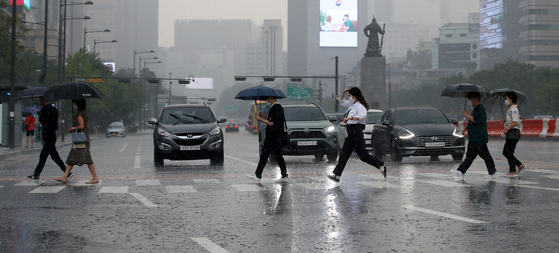 People cross a pedestrian walk in Gwanghwamun, central Seoul, on Monday, when heavy rainfall alternated with scorching heat. [NEWS1]