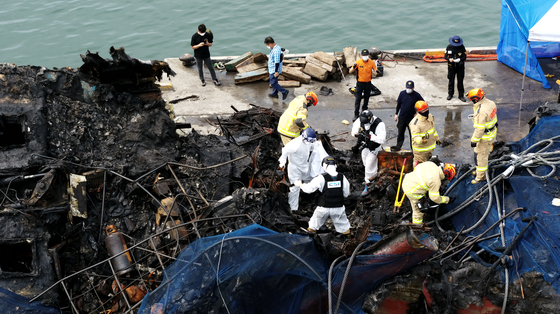 Coast Guard officials and firefighters search one of the boats from last week's fire accident in Jeju for the bodies of missing crew members. [YONHAP]