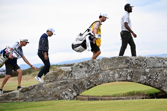 Kim Si-woo, second from left, Sahith Theegala of the United States, far right, and their caddies walk over the Swilcan Bridge on the 18th hole during the third round of The 150th British Open Golf Championship on The Old Course at St Andrews in Scotland on Saturday. [AFP/YONHAP]