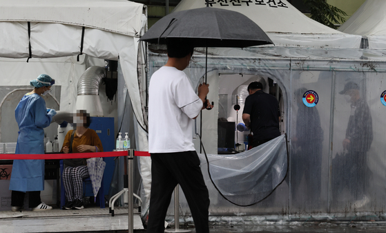 People wait in line to get tested at a testing center in Jin District, Busan, on a rainy day on Monday. [SONG BONG-GEUN]