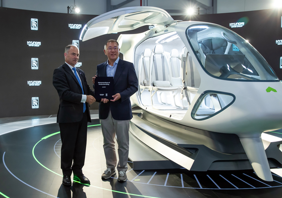 Hyundai Motor Group Chairman Euisun Chung, right, and Rolls-Royce CEO Warren East, standing next to an electric aircraft concept model made by Supernal that is expected to be introduced in 2028, pose for a photo after signing a memorandum of understanding to cooperate on the development of air mobility. [HYUNDAI MOTOR] 