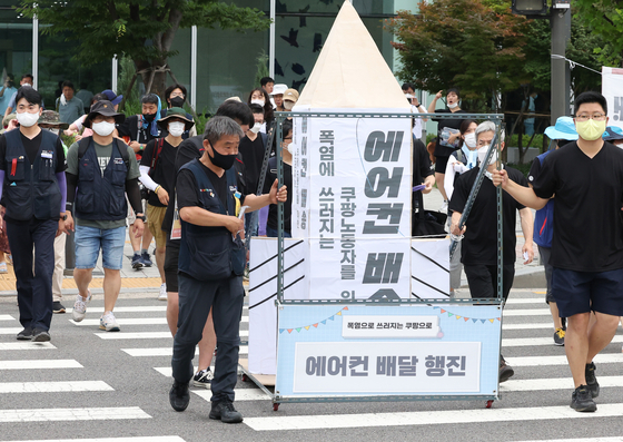 Unionized workers participate in a protest march to demand cooling devices be installed at fulfillment centers, carrying an air conditioner from Coupang’s office in Jamsil, southern Seoul, to its fulfillment center in Dongtan, Gyeonggi, on July 20. The workers attempted to occupy Coupang’s office following the protest, which the company plans to take legal action against. [YONHAP]