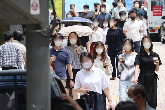 People in masks walk down the street in Myeong-dong, central Seoul, on Wednesday, as the government announced that more than 100,000 people tested positive for the coronavirus the day before. [YONHAP]