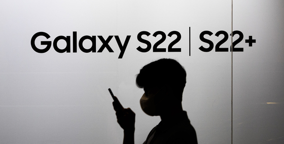 A passerby stares at their smartphone in front of the Galaxy S22 logo at the offices of Samsung Electronics in Seoch District, southern Seoul. [YONHAP]