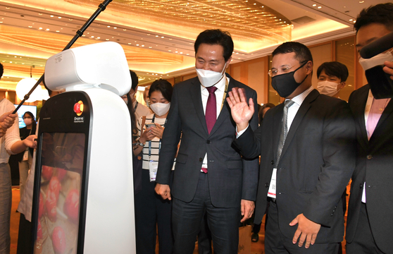 Seoul Mayor Oh Se-hoon, left, and Singapore's National Development Minister Desmond Lee look at the guide robot "Chloe" made by a Korean company at the Seoul Exhibition booth at the World Cities Summit on Sunday. [SEOUL METROPOLITAN GOVERNMENT]