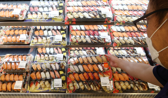 A man picks up a tray of sushi at an Emart branch in Seongsu-dong, eastern Seoul, on Wednesday. Ready-to-eat food has become popular amid the heightening inflation, with consumers preferring cheaper retail options over eating out at restaurants. July sales of ready-to-eat food products such as sandwiches and gimbap rose by 25 percent compared to the same period last year, according to Emart. [YONHAP]
