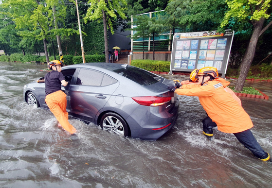 Firefighters in Incheon push a car to safety on Monday after heavy rains pounded the Seoul metropolitan area and Gangwon. [YONHAP]