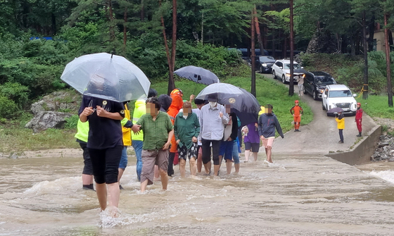 People trapped in a mountainside camping ground ijn Gangneung, Gangwon wade their way across a flooded road out of the area as the water level receded on Thursday. [YONHAP]