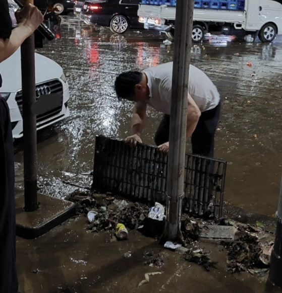 A man clears out the garbage blocking a drain on the roadside in Gangnam District, southern Seoul, Monday. [SCREEN CAPTURE]