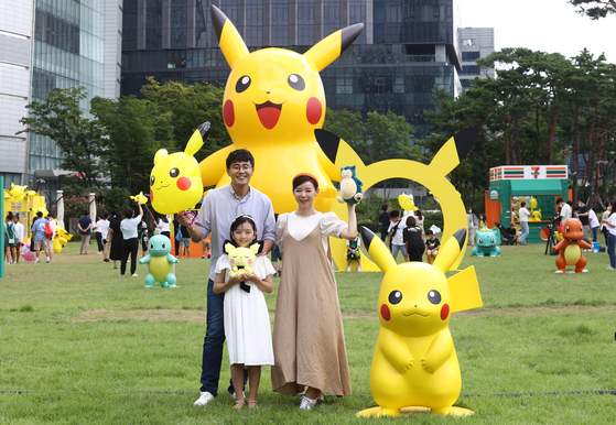 Models pose with a plastic model of the popular Japanese animated character Pikachu and a 50-foot-tall Pikachu balloon figure on the back on the lawn of Lotte Tower in Jamsil, southern Seoul, on Tuesday. The convenience store 7-Eleven announced Tuesday that a “Smiling Pokemon” play zone will be opened until Sept. 12. It will also have a pop-up store selling Pikachu-themed products including omurice in a package shaped like the face of Pikachu as well as Pokemon spaghetti and key rings. [YONHAP] 
