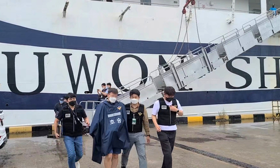 Policemen escort two criminal suspects off a passenger ship in Donghae Port in Gangwon on Wednesday. The two suspects fled to Russia after allegedly committing crimes in Korea.   [NEWS1]