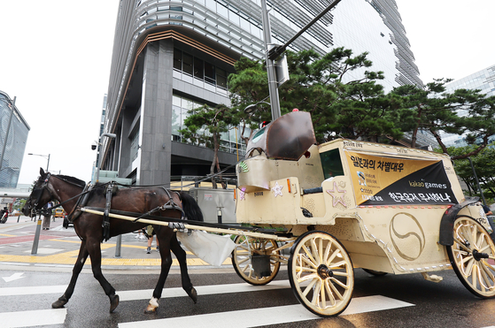 A horse-drawn carriage criticizing Kakao Games' Uma Musume Pretty Derby mobile game takes a spin around the Pangyo neighborhood in Gyeonggi, where Kakao Games is located, on Monday. The game, which revolves around personified race horse girls, is developed by Japanese company Cygames and published by Kakao Games. Users have been complaining of the publisher squeezing money from players and operating the game differently from how it is in Japan. [YONHAP]